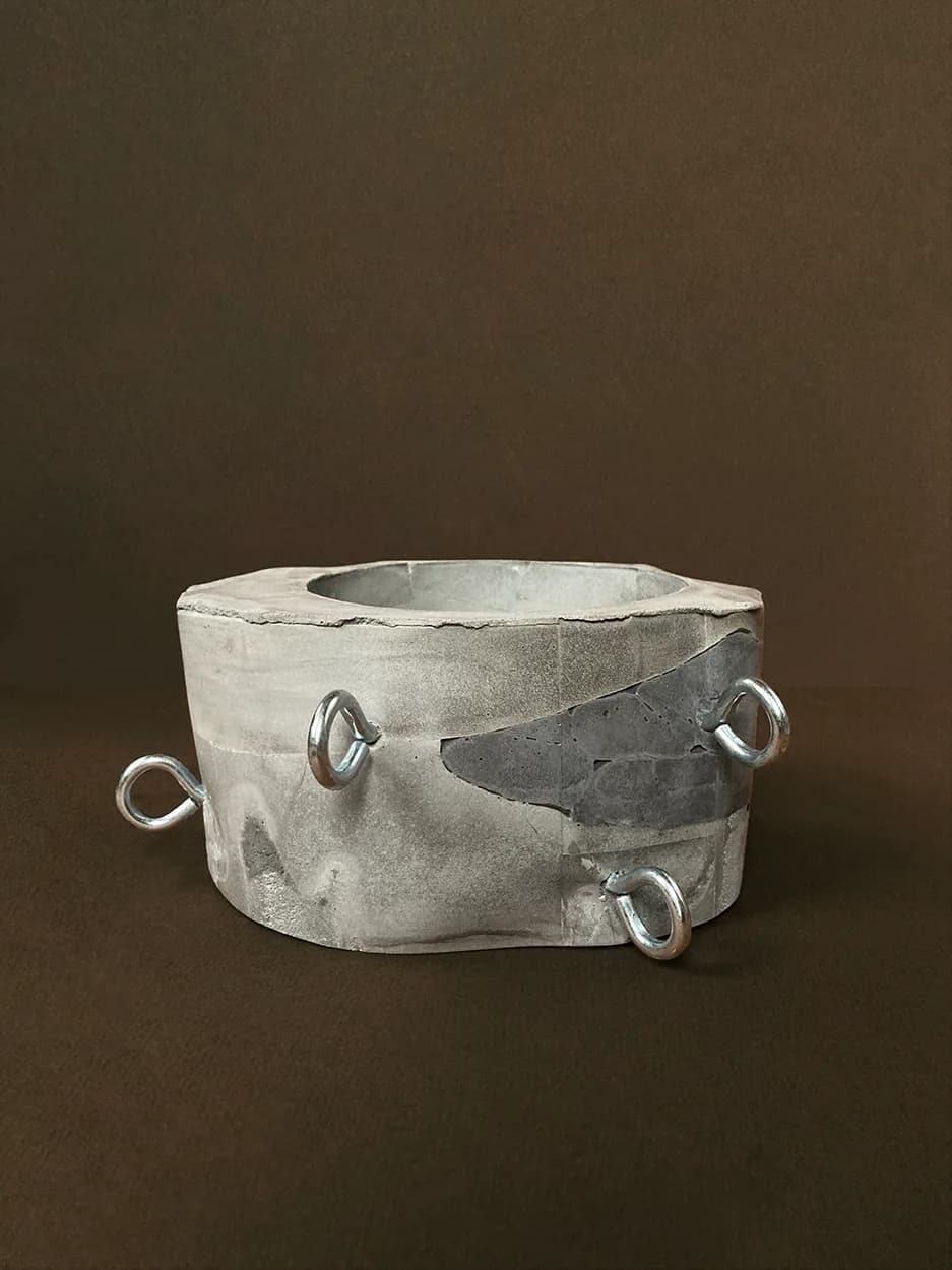 Run Your Finger Over My Hoops — a faceted concrete vessel with three chrome rods, unplanted